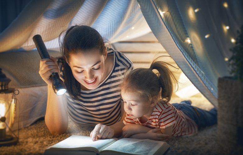 A woman and a child read a book while using a flashlight.