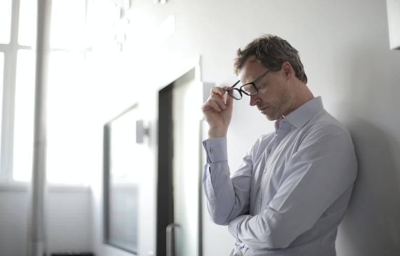 man holding black eyeglasses thinking deeply