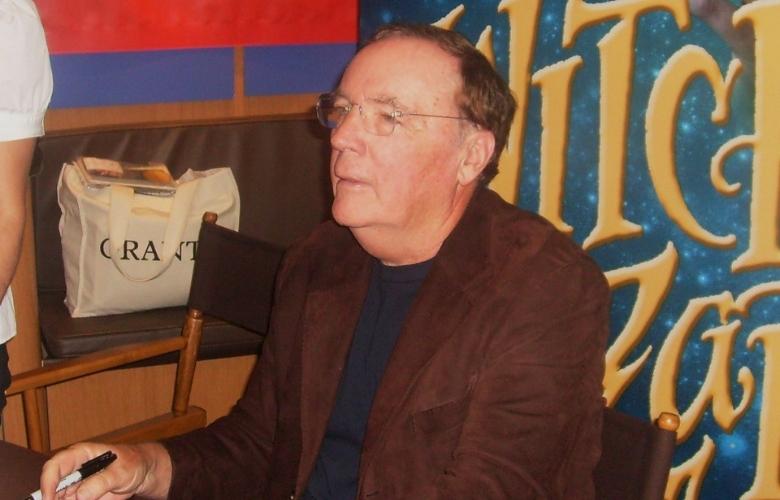 this image of james patterson signing books features the witch and wizard book cover as a backdrop